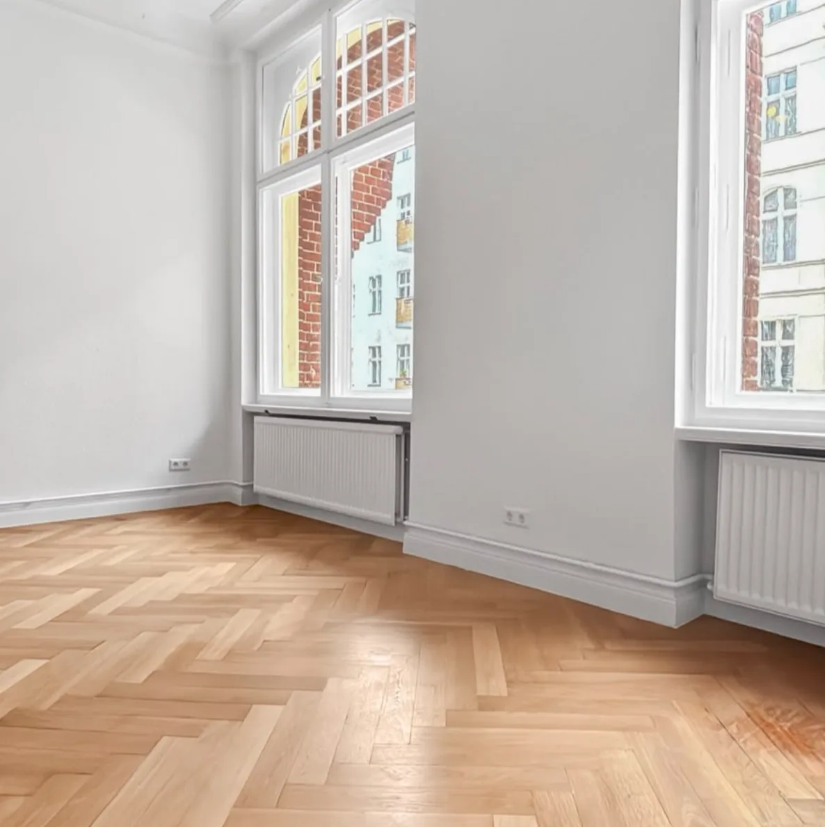 Eckzimmer einer Berliner Altbauwohnung mit Fischgrätparkett und profilierten Berliner Sockelleisten