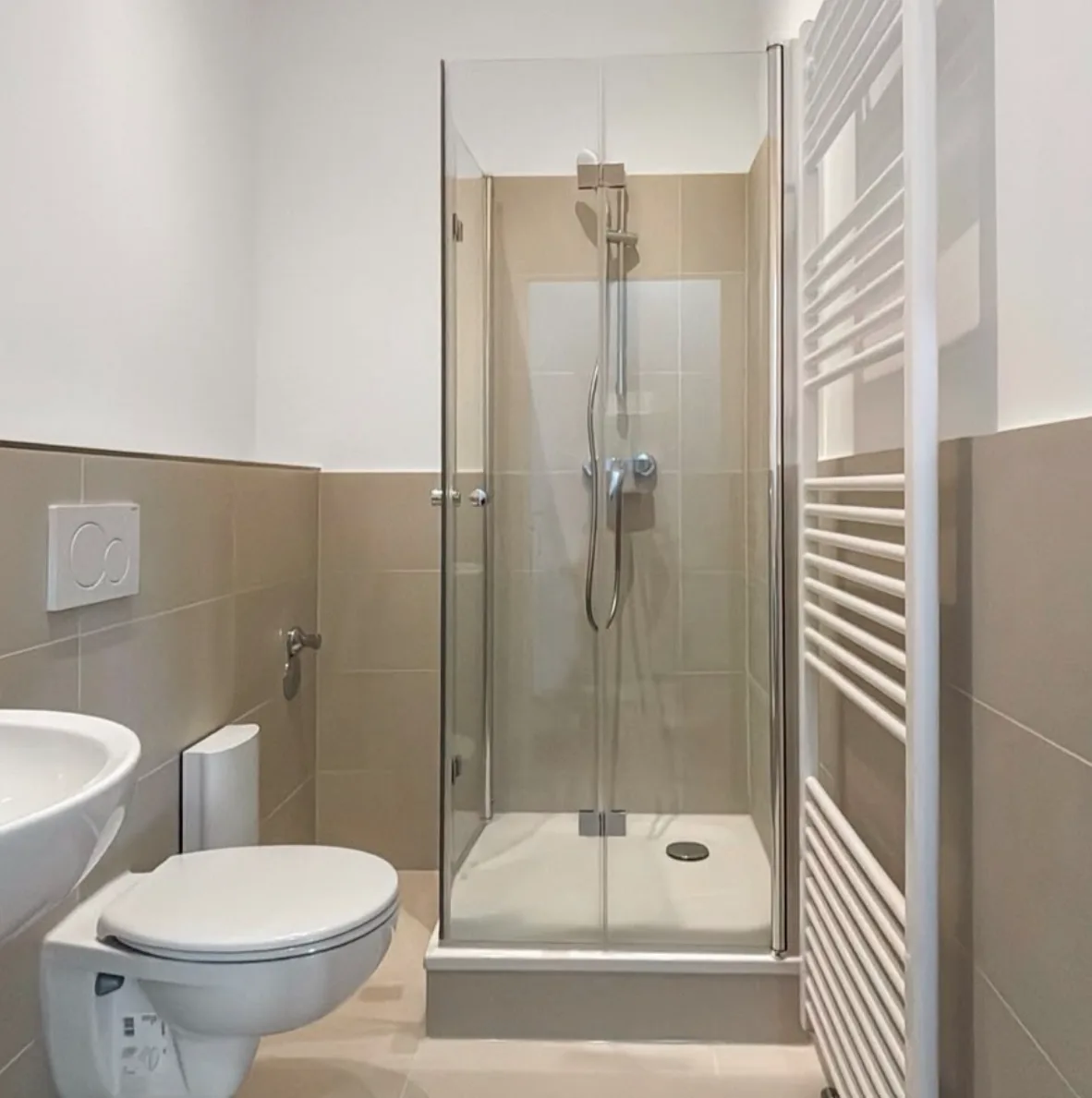 Eck-Duschkabine mit Echtglas-Falttüren neben Wand-WC und Handtuchheizkörper